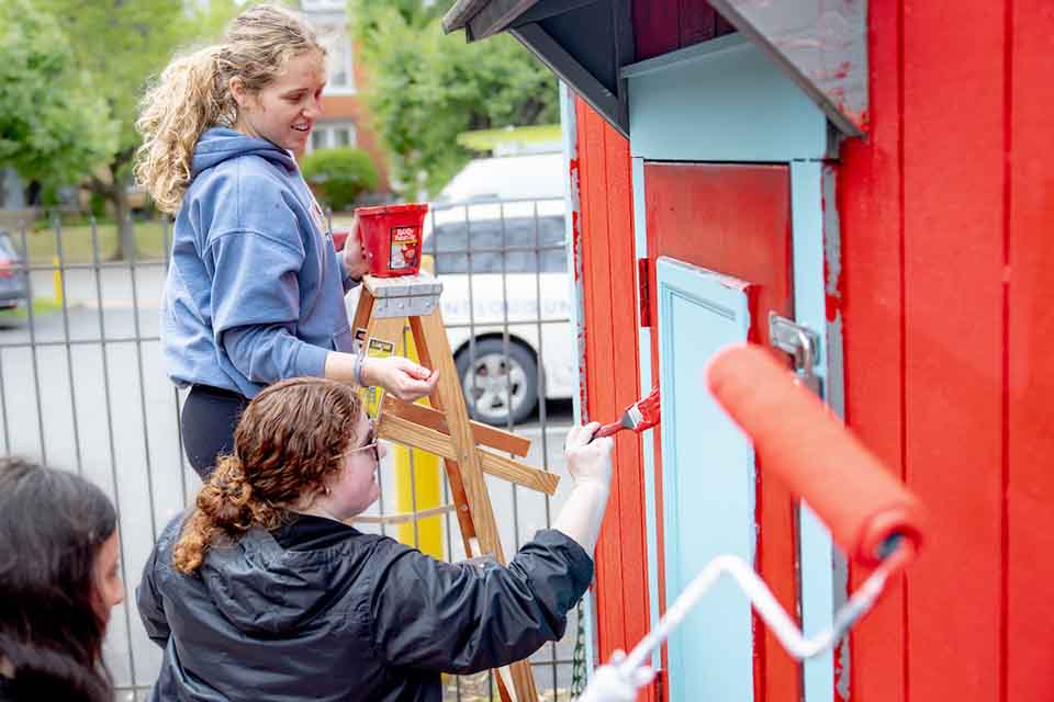 Students volunteering painting an outside structure during Showers of Service