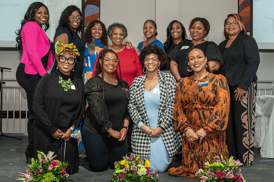 A group of 12 women pose for a photo on a stage.