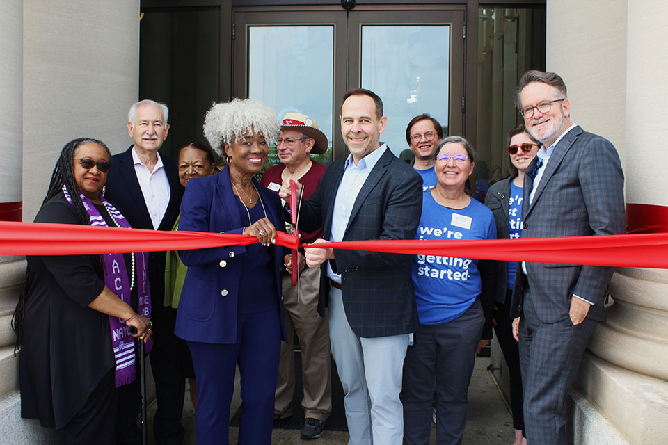 A group of Missouri History Museum staff and partners pose for a photo cutting a large ribbon.