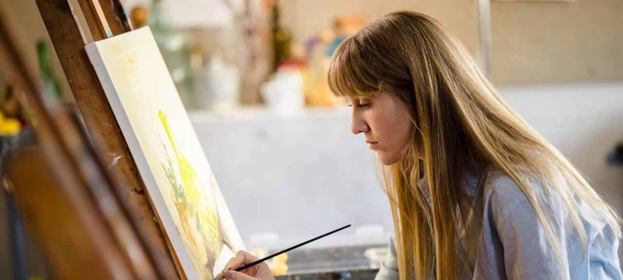 A female visual and performing arts student paints in a classroom.