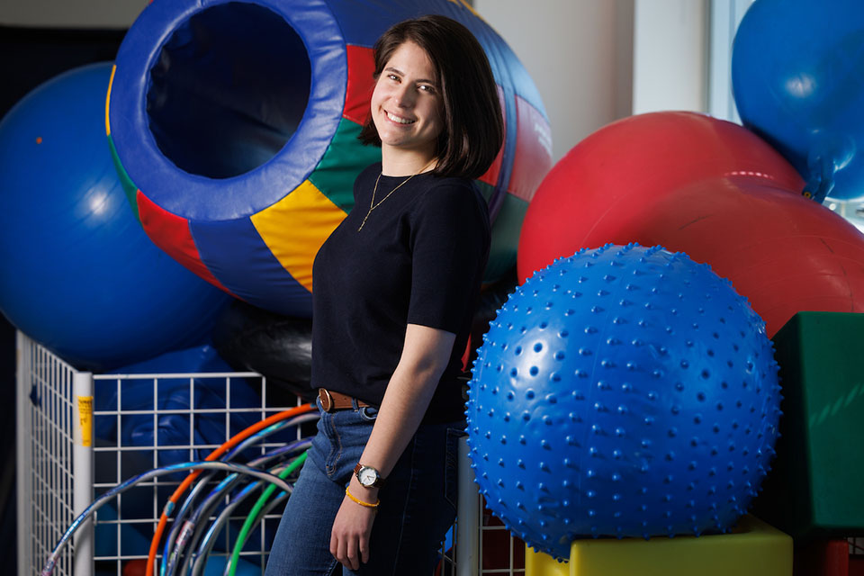 Mariangela Acosta poses for a photo next to a bin of colorful hula hoops, balls and cubes.