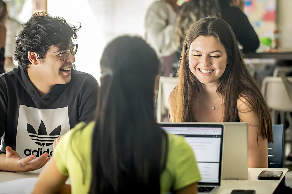 Two students talk and smile while looking at a laptop