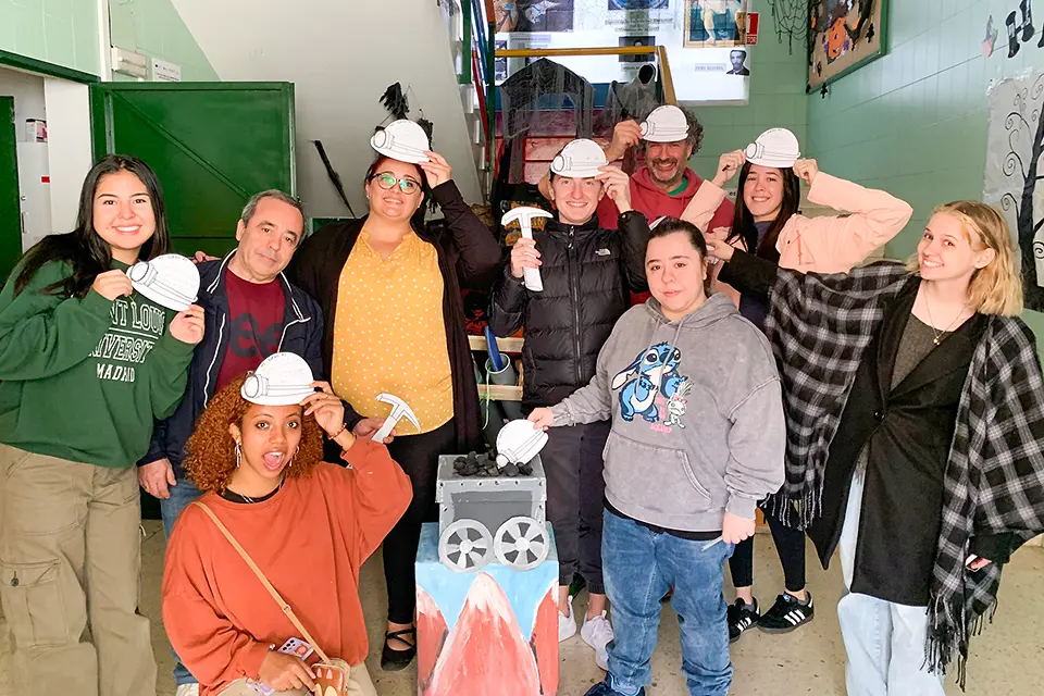 Students and professor smile while holding up cardboard cut outs of construction hats to their heads and hammers.