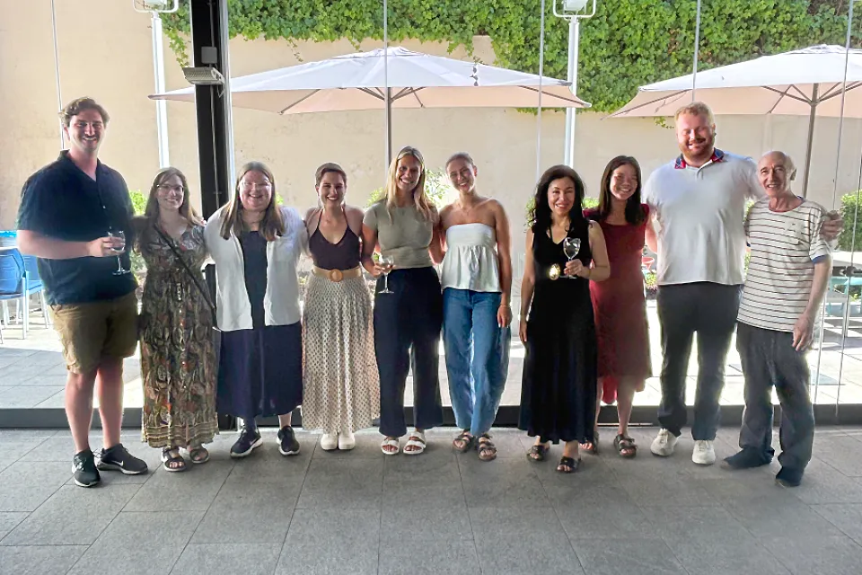 A group of people pose for a photo with a courtyard seen through glass doors behind them. 
