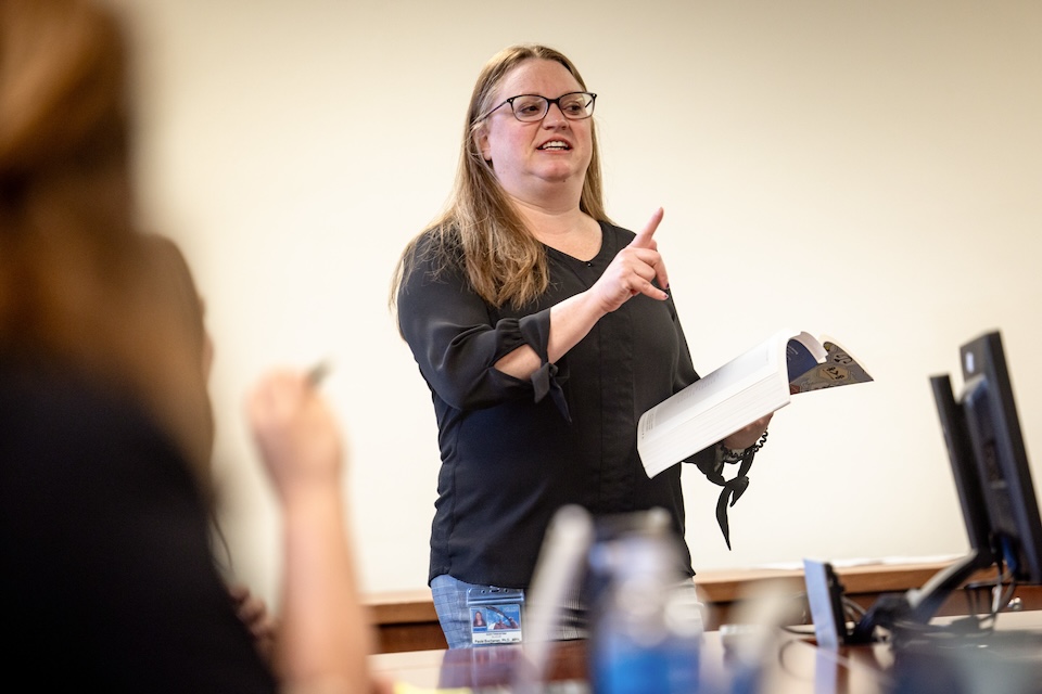 A female professor teaches in a classroom full of students.