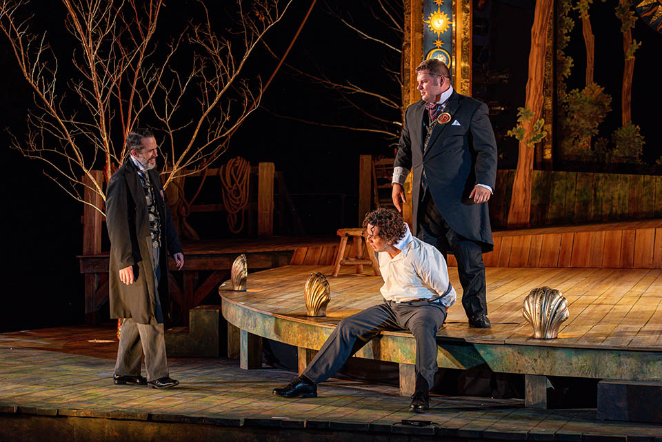 Three men perform on a stage in a dimly lit room.