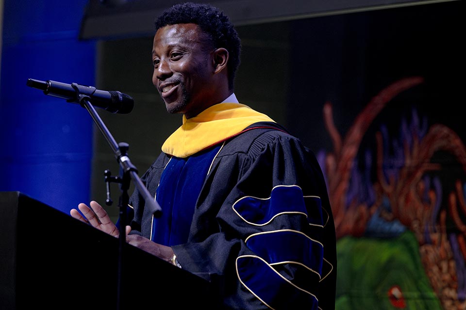 a man in graduation clothes stands in front of a podum smiling