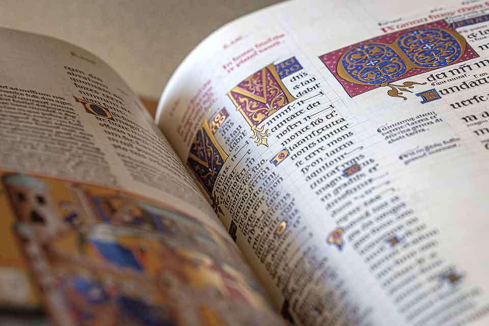 A close-up image of an illuminated manuscript. Ornate gold, red, and blue symbols decorate the pages.