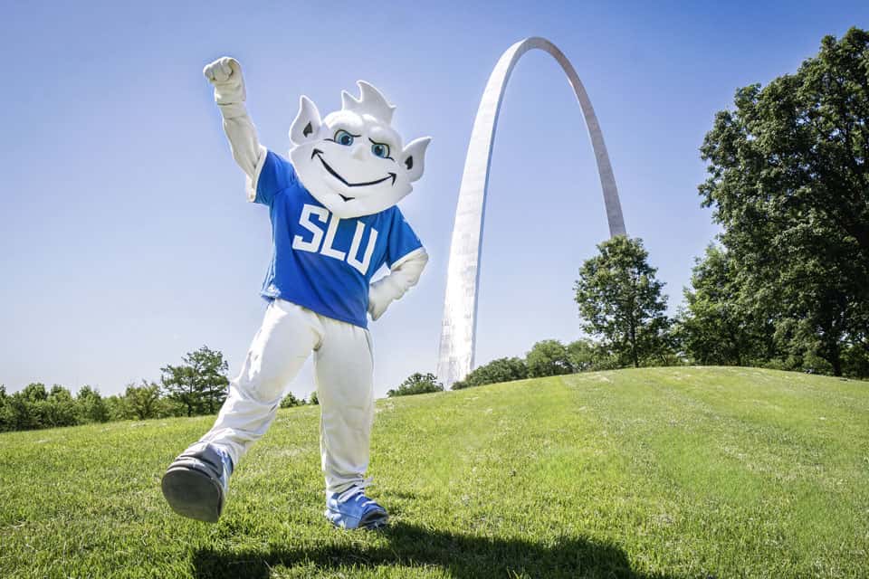 SLU Billiken mascot on the green grass in front of the st louis gateway arch
